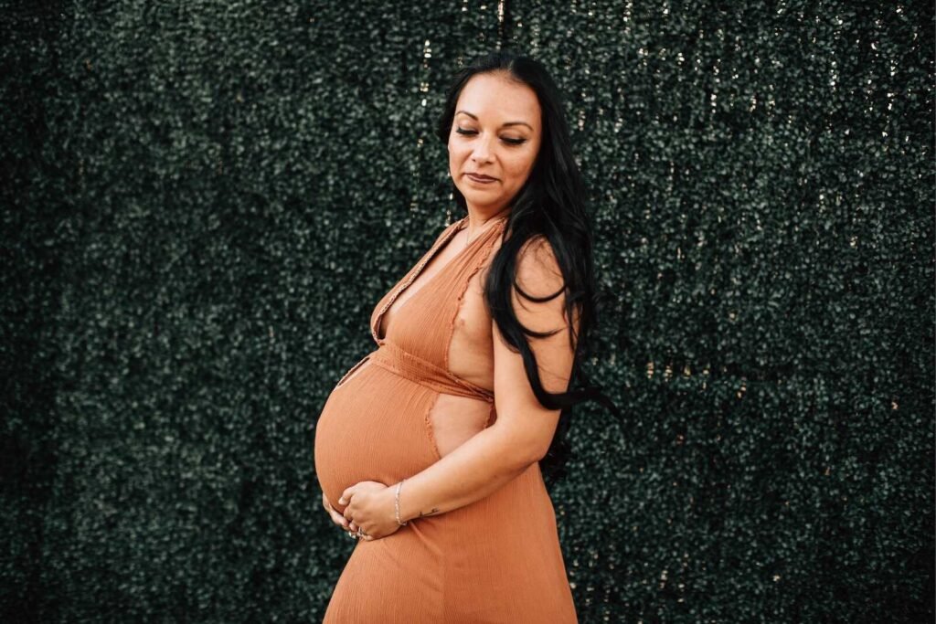 Pregnant woman in a rust orange dress posing outdoors showing what to wear to a maternity photo shoot.