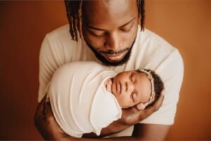 Father holding swaddled newborn illustrating when to do newborn photos