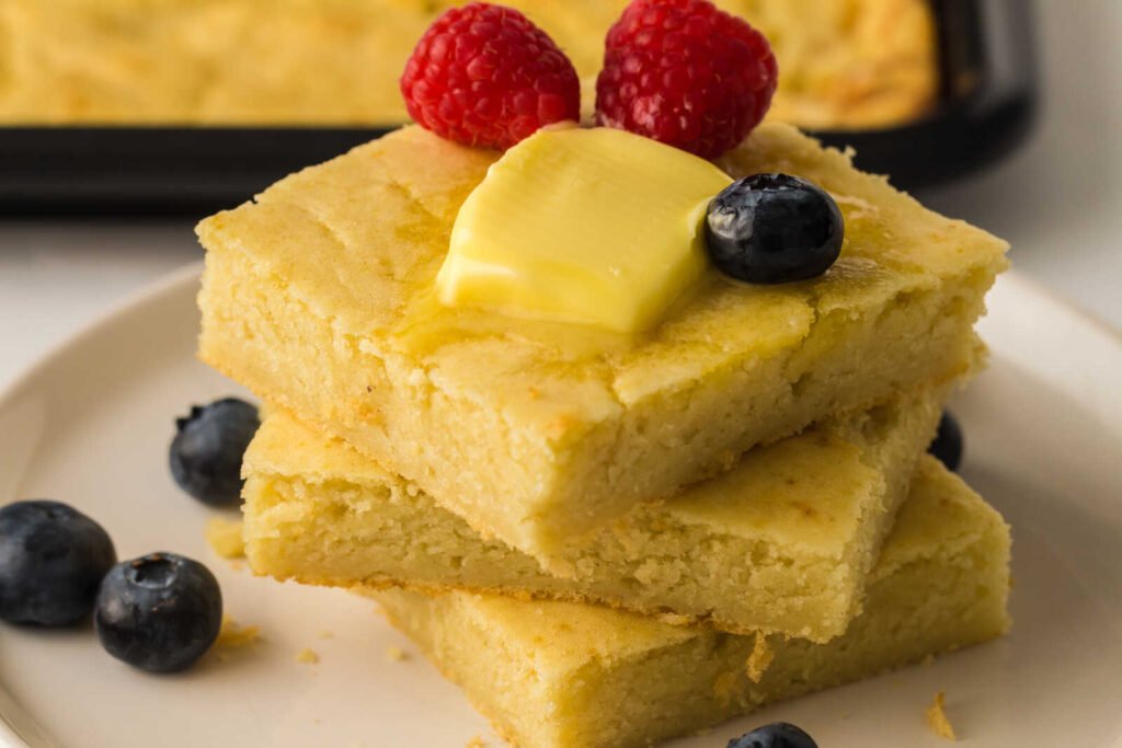 Sheet pan pancakes stacked with butter and fresh raspberries and blueberries.