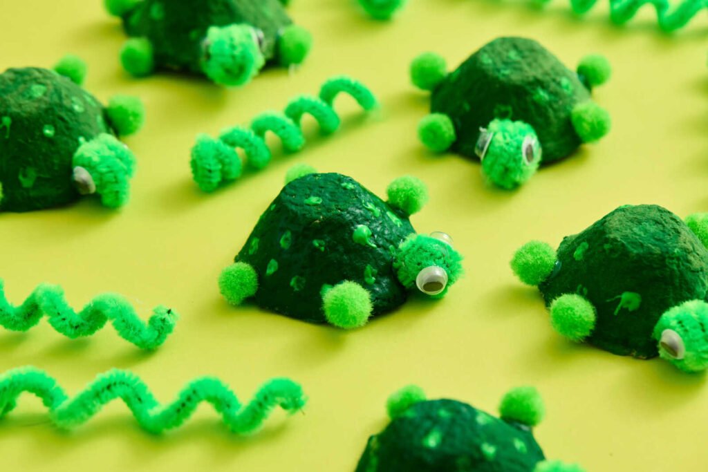 Multiple egg carton turtle craft creations with painted green shells, pom-pom legs, and googly eyes.