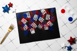 Fork-stamped 4th of July fireworks art craft with multiple red, white, and blue bursts on black paper.