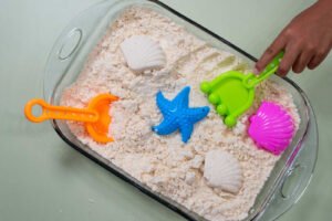 Beach play moon sand sensory bin with colorful scoops, shell molds, and a starfish toy.